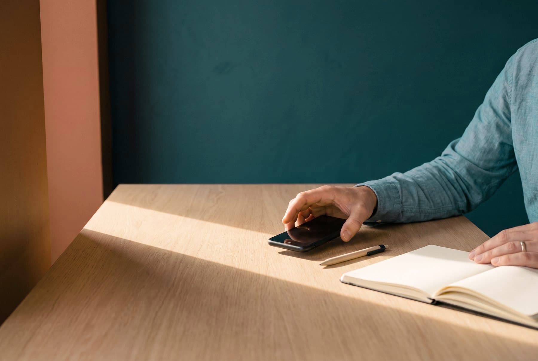 An agent's hand reaching for a phone on a desk beside an open notebook